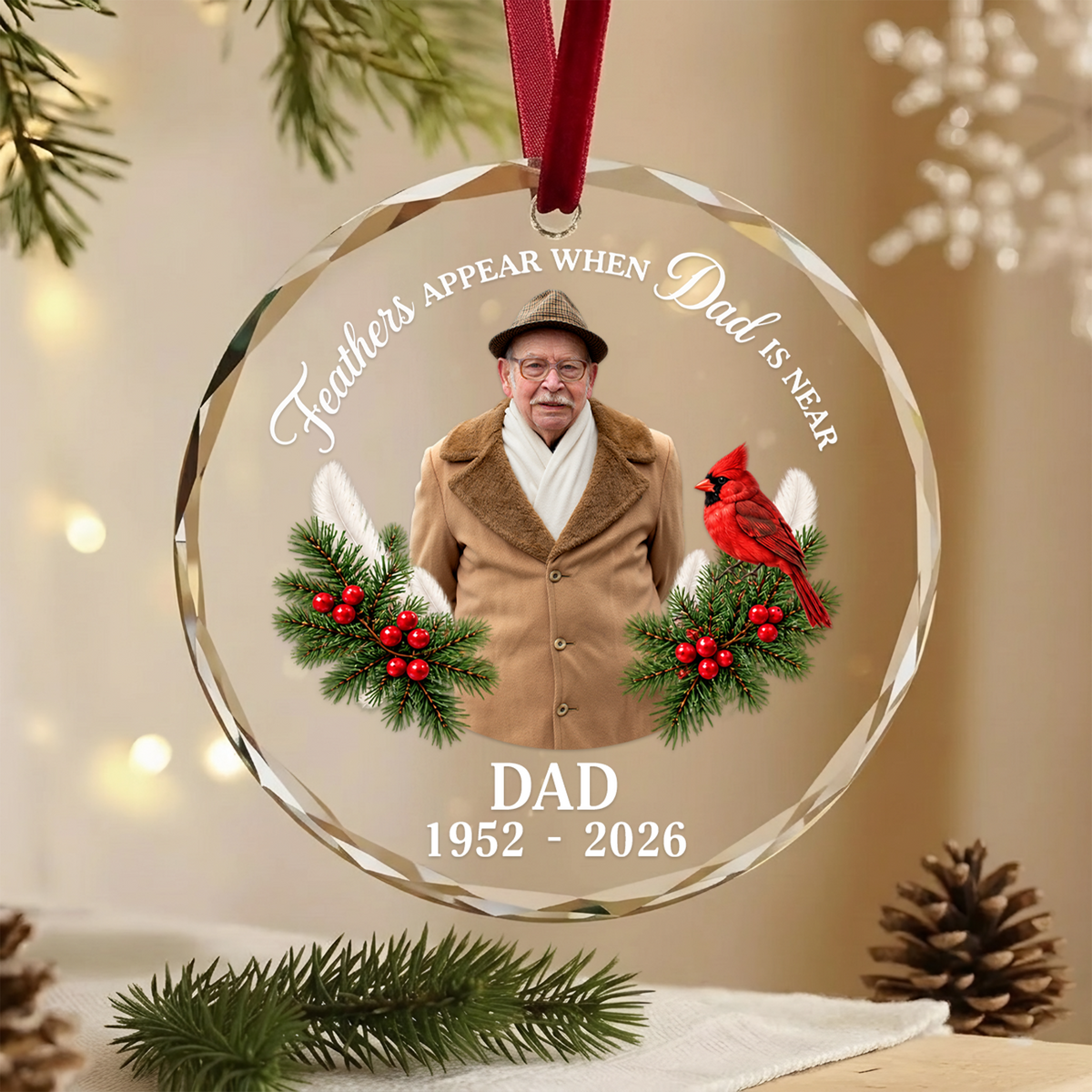 Personalized glass ornament custom photo hanging on red ribbon beside pine branch and pinecone