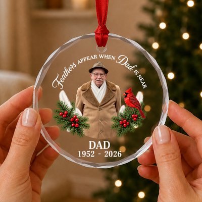 Personalized glass ornament custom photo held between two hands in front of lit Christmas tree