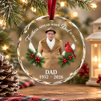 Personalized glass ornament custom photo hanging near a pinecone, plaid cloth and lantern on a wooden table