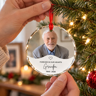 Personalized glass ornament custom photo held by hand on a red ribbon near a tree and candle