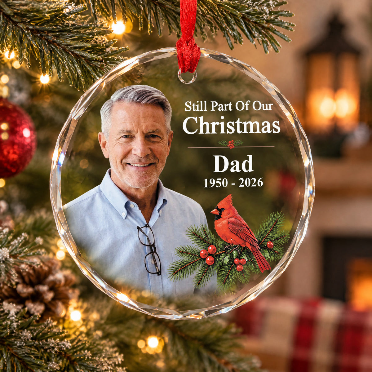 Personalized glass ornament custom photo hanging on a tree with a pine cone and a fireplace glowing behind