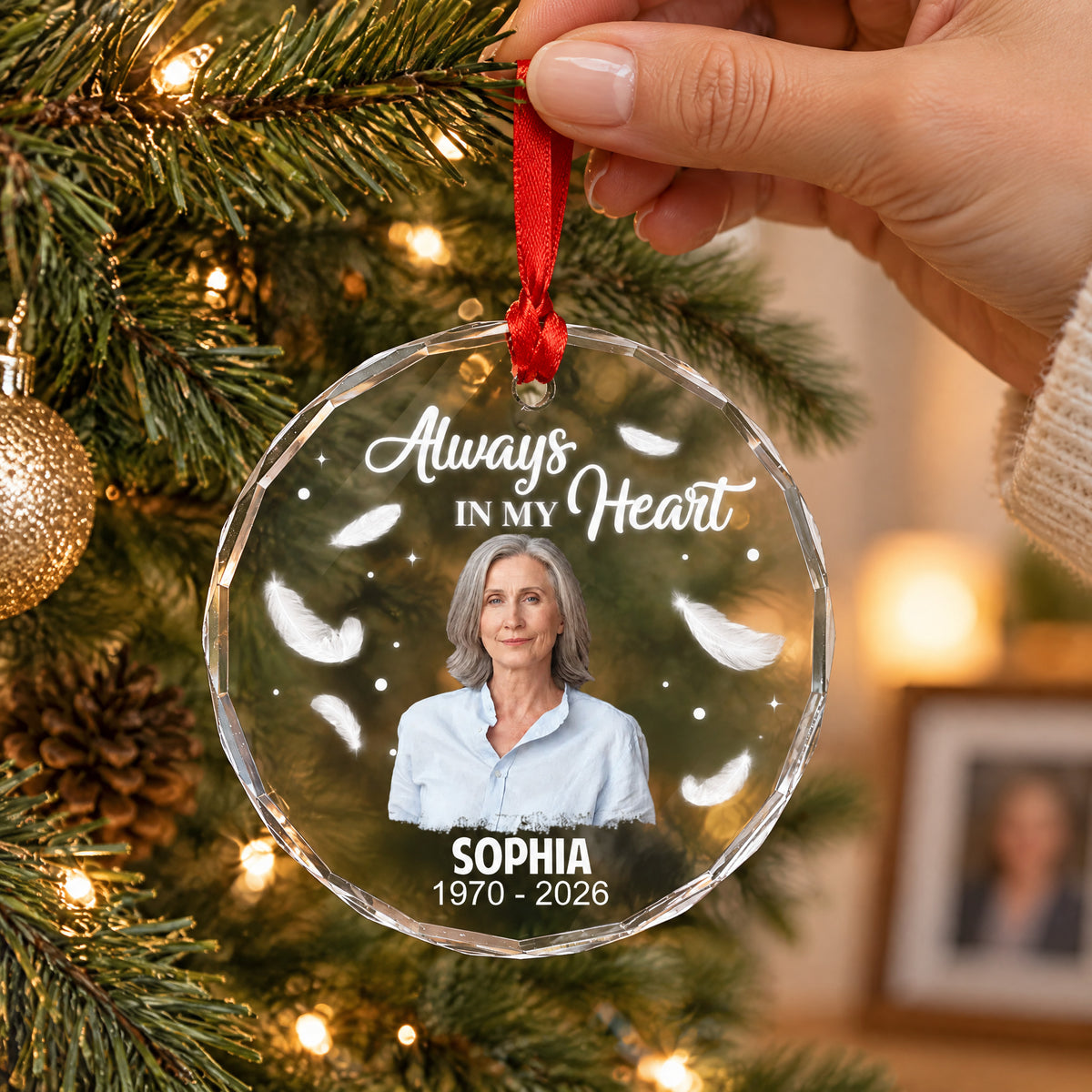 Personalized Glass Ornament Always In My Heart held by hand on a lit tree, woman's photo, feathers and dates
