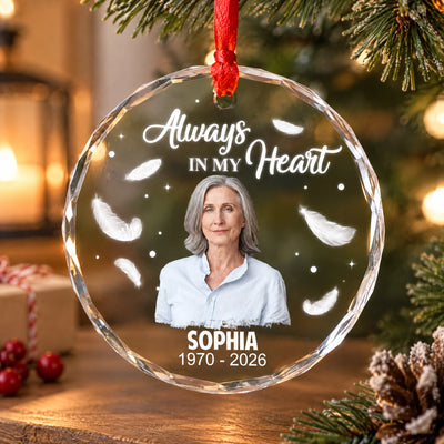 Personalized Glass Ornament Always In My Heart hanging on a tree with candle, gift box and pinecone, woman's photo shown