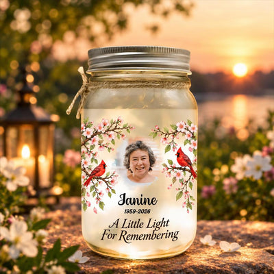 Personalized Mason Jar Light glowing on a stone ledge with blossoms, a lantern and a sunset behind