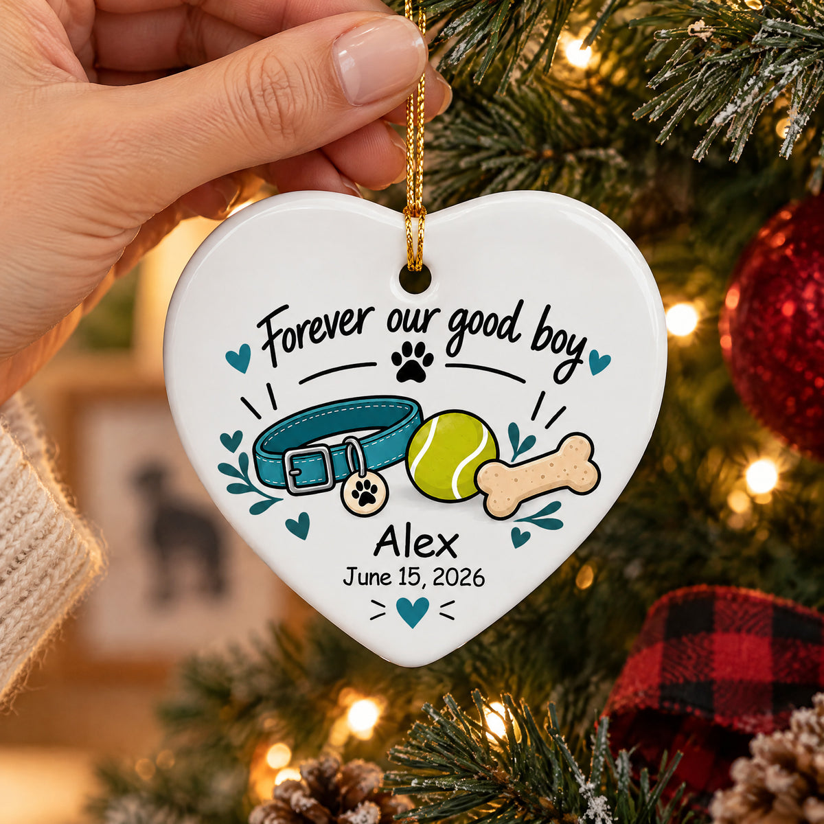 Personalized ceramic ornament Forever Our Good Boy held by a hand beside a tree with red baubles