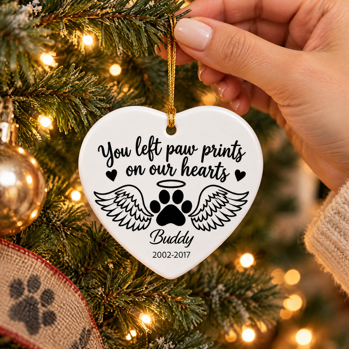 Personalized ceramic angel wings pet memorial ornament held by a hand in front of a lit Christmas tree