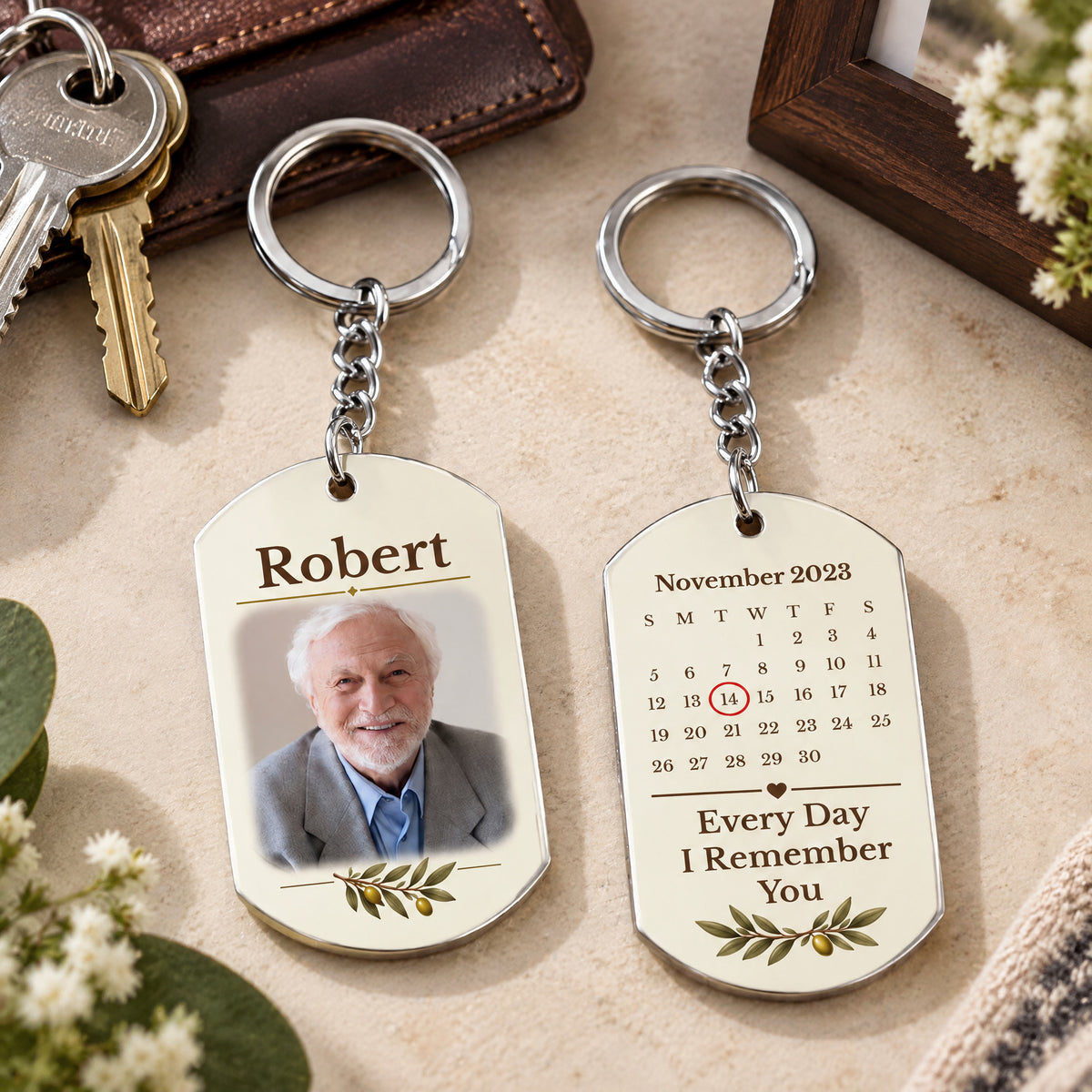 Personalized stainless steel memorial keychain pair on a light surface with house keys, a wallet and white flowers