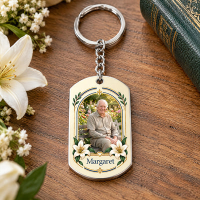 Personalized Stainless Steel Keychain with photo, name and lily arch frame, resting on wood beside white flowers and a book